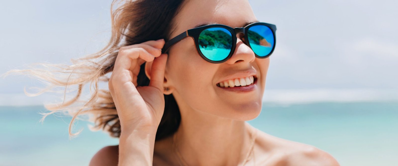 Spectacular girl in trendy sparkle sunglasses enjoying good day at ocean resort. Outdoor portrait of sensual tanned woman posing at sea coast in summer morning.